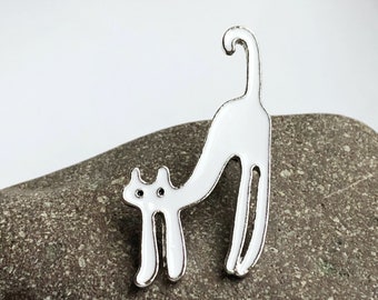 May include: White enamel pin of a stylized cat with a long tail. The cat is standing on its hind legs with its front paws outstretched.