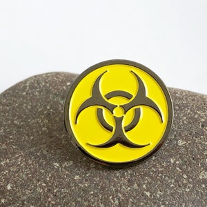 May include: A yellow and black biohazard symbol pin. The symbol is a stylised triangle with three points, each with a small circle in the centre.