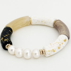 May include: A bracelet made of black, white, and beige beads with gold flecks. The bracelet is accented with five white pearls.
