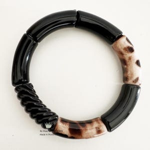 Puede incluir: Pulsera negra y marrón hecha de cuentas redondas. La pulsera tiene una cuenta negra retorcida y una cuenta con estampado de leopardo.