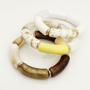 Può includere: Tre braccialetti in resina bianca, gialla e marrone con glitter dorati. I braccialetti sono impilati uno sopra l'altro. Il testo "By Dom Creations Made in Provence" è visibile sul braccialetto inferiore.