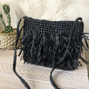 May include: Black woven crossbody bag with a fringe detail. The bag has a long strap and is made of a natural material.