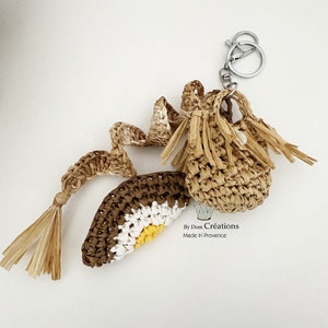 May include: A collection of woven raffia accessories, including a small pouch with a silver keychain, a decorative element, and a crocheted piece with brown, white, and yellow stripes. The accessories are handmade.