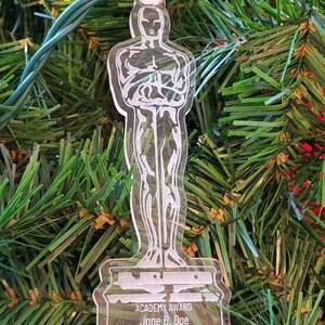 Puede incluir: Un adorno de pl&aacute;stico transparente con forma de estatuilla de los Oscar. El adorno tiene el texto "ACADEMY AWARD" y "Jane B. Doe" en la base. El texto "Best Sarcastic Performance 2022" tambi&eacute;n est&aacute; en la base.