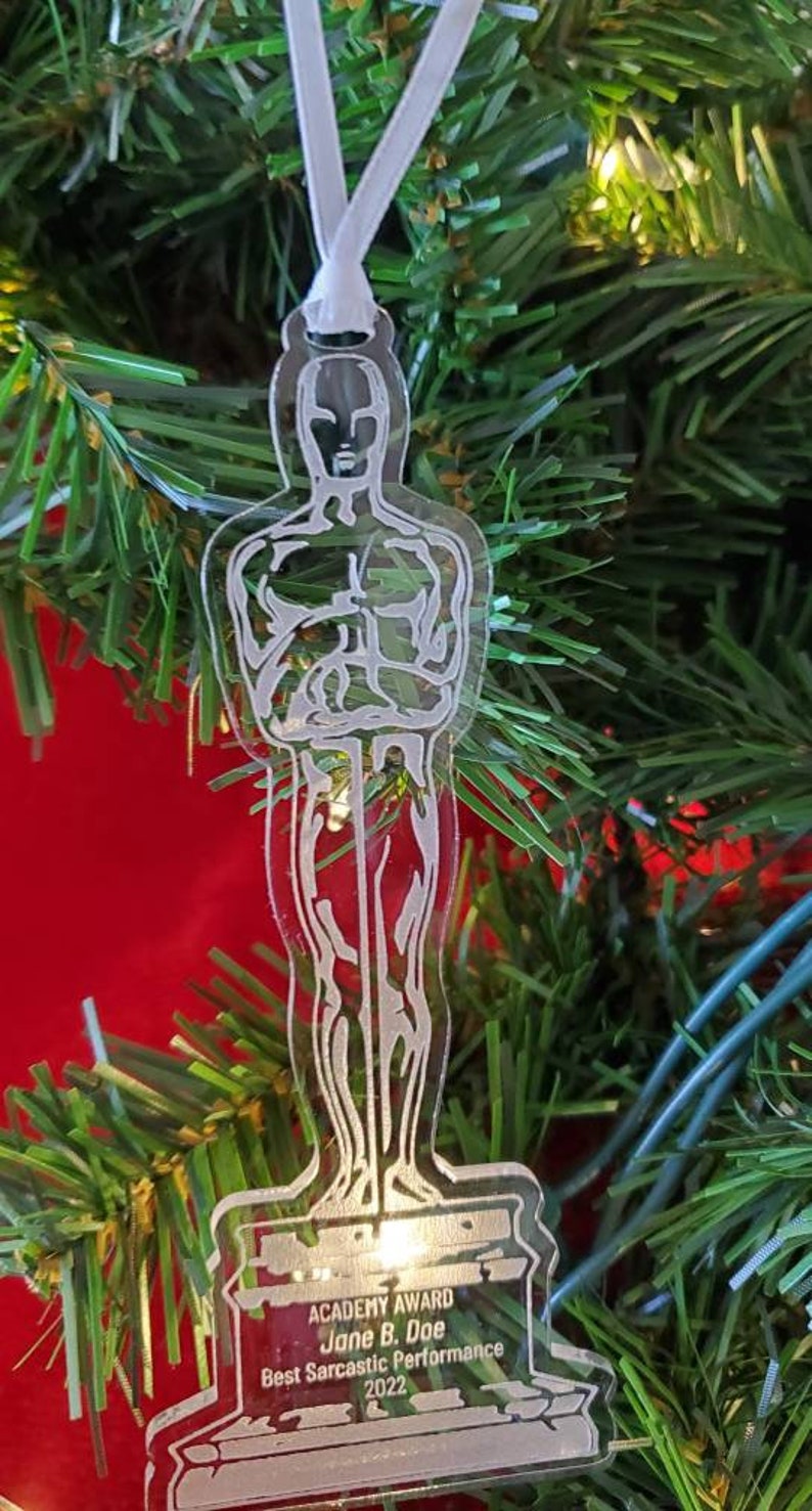 Puede incluir: Un adorno de pl&aacute;stico transparente con forma de estatuilla de los Oscar. La base del adorno dice "Academy Award Jane B. Doe Best Sarcastic Performance 2022".
