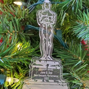Puede incluir: Un adorno de acr&iacute;lico transparente con forma de la estatuilla del Premio de la Academia. La base del adorno dice "ACADEMY AWARD Jane B. Doe Best Sarcastic Performance 2022".
