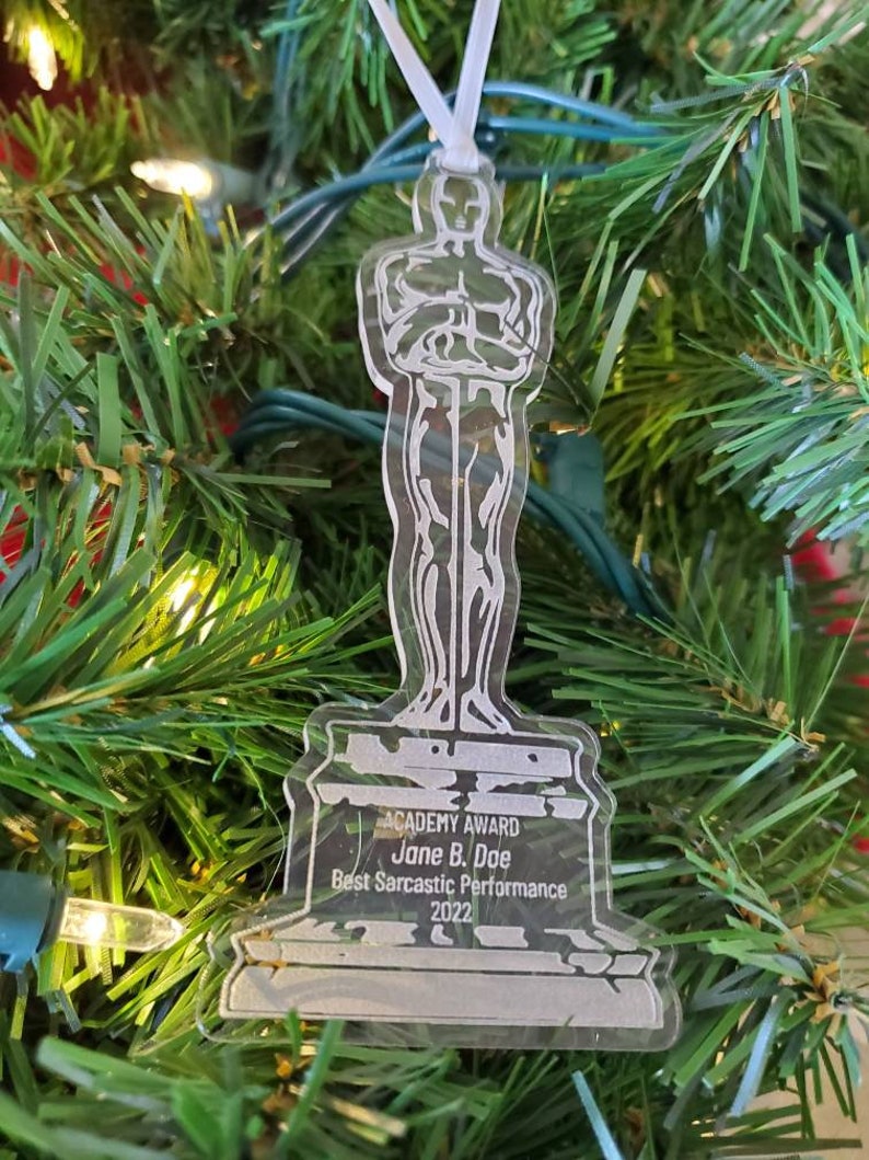 Puede incluir: Un adorno de acr&iacute;lico transparente con forma de la estatuilla del Premio de la Academia. La base del adorno dice "ACADEMY AWARD Jane B. Doe Best Sarcastic Performance 2022".