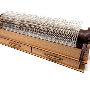 May include: A wooden storage box with two drawers and a clear plastic cylinder with a brown wooden base. The cylinder is filled with clear plastic pins.