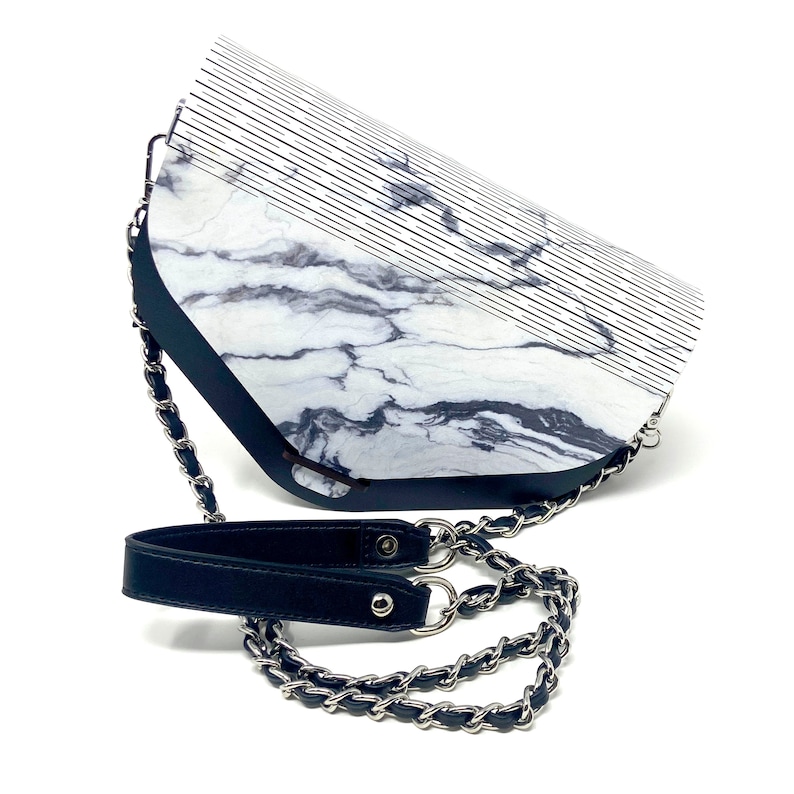 Puede incluir: Un bolso de mano blanco y negro con estampado de m&aacute;rmol, con una correa de cuero negro y una correa de cadena plateada.