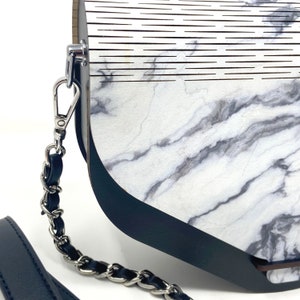 Puede incluir: Un bolso de mano con estampado de m&aacute;rmol blanco y negro, ribete de cuero negro y correa de cadena plateada.