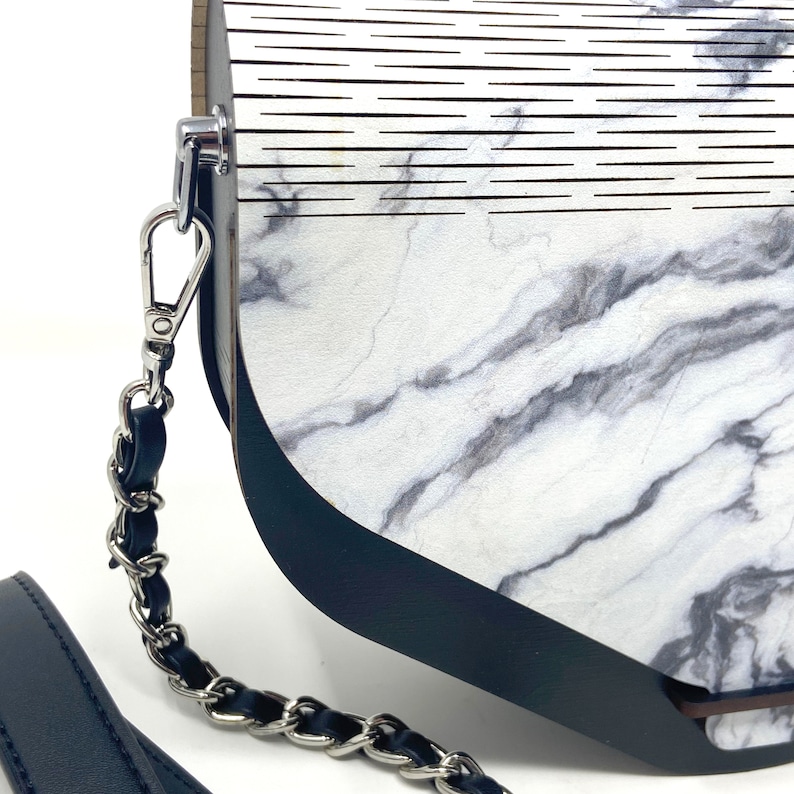 Puede incluir: Un bolso de mano con estampado de m&aacute;rmol blanco y negro, ribete de cuero negro y correa de cadena plateada.