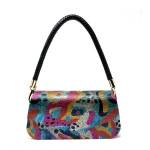 May include: A small, colorful handbag with a black braided strap. The bag has a glittery, abstract pattern in shades of pink, blue, gold, and silver.