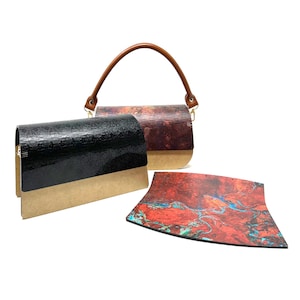 Può includere: Due borse a mano in legno con manico in pelle marrone. Una borsa a mano è nera con fondo marrone e l'altra è rossa, arancione e blu con fondo marrone. È mostrato anche un pezzo di legno rosso, arancione e blu.
