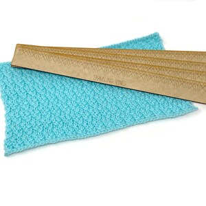 May include: A set of four wooden knitting row counters with the text "TRAVELING VINES" printed on them. The counters are stacked on top of a light blue knitted fabric.