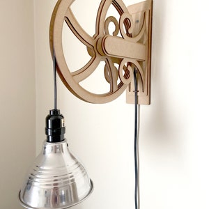 May include: A wooden wall-mounted light fixture with a pulley design and a silver metal lampshade. The fixture has a black cord and a black electrical socket.