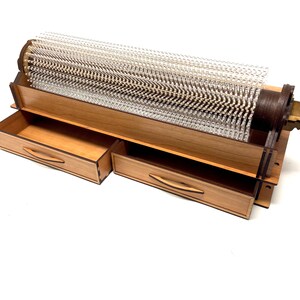 May include: A wooden box with two drawers and a clear plastic cylinder with a wooden base and a metal knob. The cylinder is filled with small, clear plastic rods.