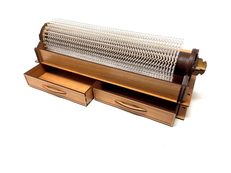 May include: A wooden box with two drawers and a clear plastic cylinder with a wooden base and a metal knob. The cylinder is filled with small, clear plastic rods.