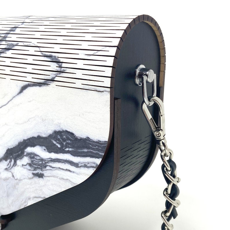 Puede incluir: Un bolso de mano de madera negra con estampado de m&aacute;rmol blanco y negro y una cadena plateada.