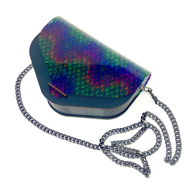 Puede incluir: Un peque&ntilde;o bolso de mano iridiscente negro, verde y azul con una correa de cadena. El bolso tiene una forma geom&eacute;trica y un patr&oacute;n de escamas.