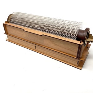May include: A wooden box with a clear plastic grid inside. The box is made of light wood with dark brown trim. The grid is made of clear plastic and has a series of small holes.