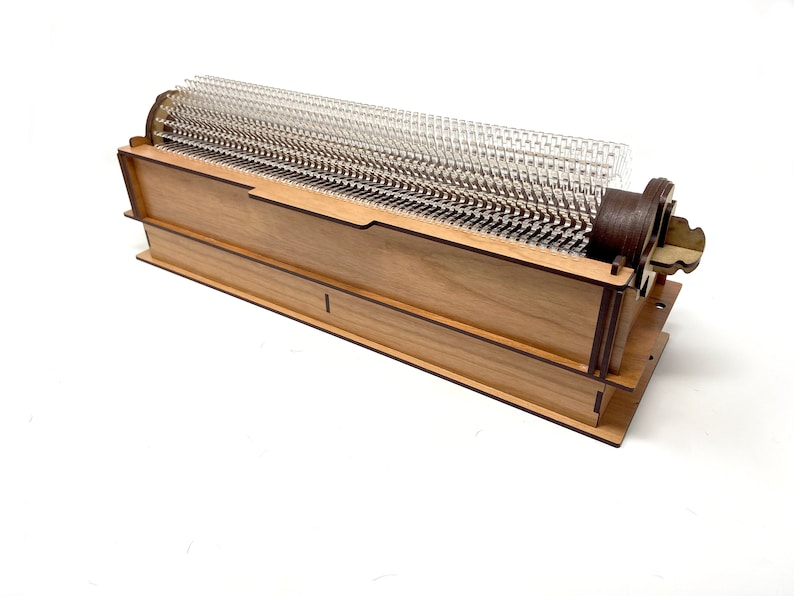 May include: A wooden box with a clear plastic grid inside. The box is made of light wood with dark brown trim. The grid is made of clear plastic and has a series of small holes.
