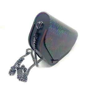 Puede incluir: Un bolso de mano negro e iridiscente con una correa de cadena. El bolso tiene una forma geom&eacute;trica &uacute;nica y un dise&ntilde;o texturizado y escamoso.