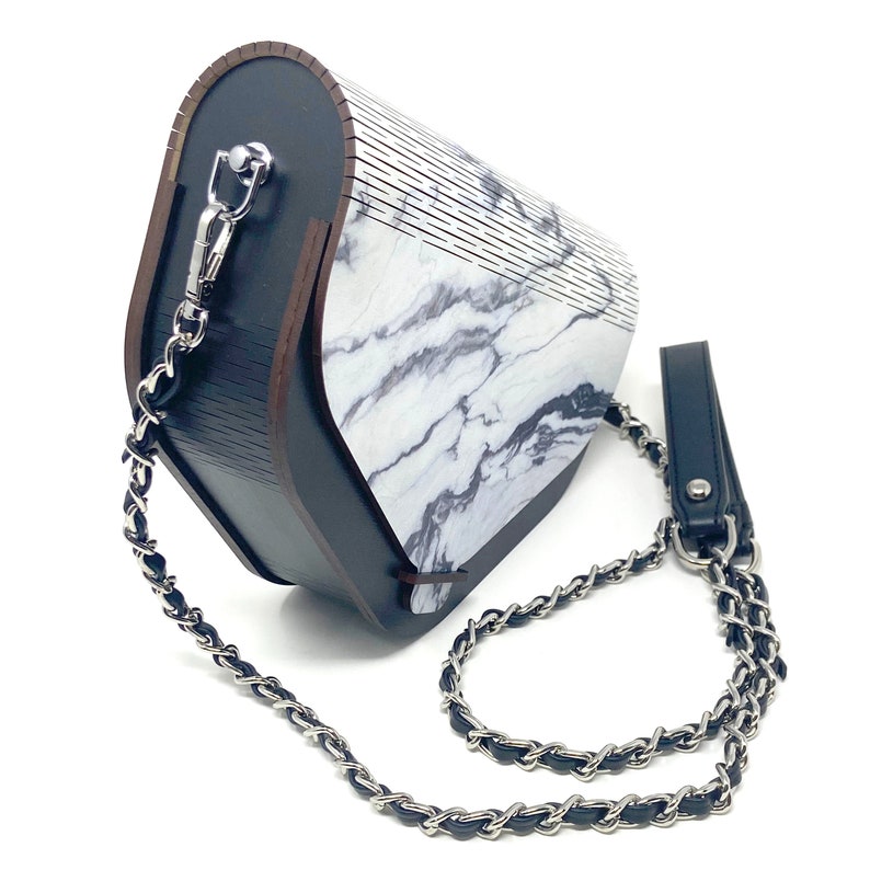 Puede incluir: Un bolso de mano con estampado de m&aacute;rmol blanco y negro con una correa de cadena negra y un asa de cuero negro.