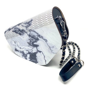 Puede incluir: Un bolso de mano con estampado de m&aacute;rmol blanco y negro con una correa de cuero negro y una correa de cadena plateada.