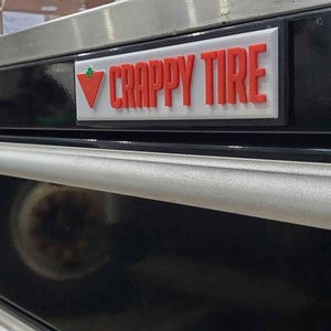 May include: A black metal toolbox with a silver handle and a red and white "CRAPPY TIRE" logo.