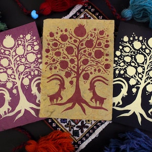May include: Three handmade cards with a gold leaf design of a pomegranate tree with goats on either side. The cards are on a dark background with a patterned rug underneath.
