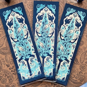 May include: Three rectangular bookmarks with a dark blue background and a light blue and white floral and bird design. The bookmarks are arranged on a brown patterned surface. The design includes birds, flowers, and other decorative elements.