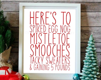 May include: White framed print with red text that reads "Here's to spiked egg nog, mistletoe smooches, tacky sweaters & gaining 5 pounds". The print is sitting on a wooden surface with small Christmas trees and ornaments.