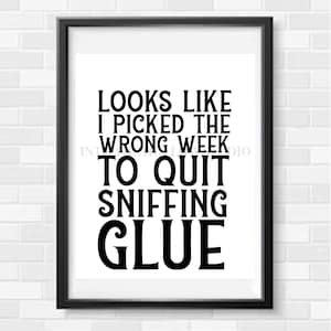May include: A framed print with a white background and black text that reads: "LOOKS LIKE I PICKED THE WRONG WEEK TO QUIT SNIFFING GLUE." The print is in a black frame and is displayed against a white brick wall.