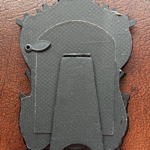 May include: Black ornate picture frame with a stand on the back. The frame has a textured surface and a small metal loop on the side.