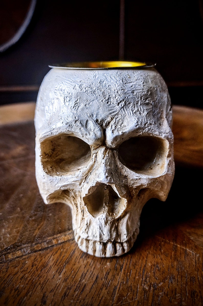 Pode incluir: Queimador de incenso de caveira de cer&acirc;mica branca com topo de metal dourado. A caveira tem um design detalhado e est&aacute; sobre uma superf&iacute;cie de madeira.