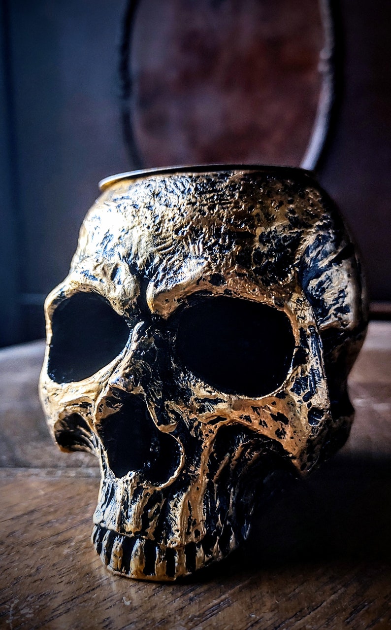 Pode incluir: Um porta-velas em forma de caveira dourado e preto. A caveira &eacute; detalhada com caracter&iacute;sticas texturizadas e uma &oacute;rbita ocular preta.