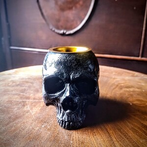 Pode incluir: Queimador de incenso de caveira preta com aro dourado. O queimador est&aacute; sobre uma mesa de madeira.