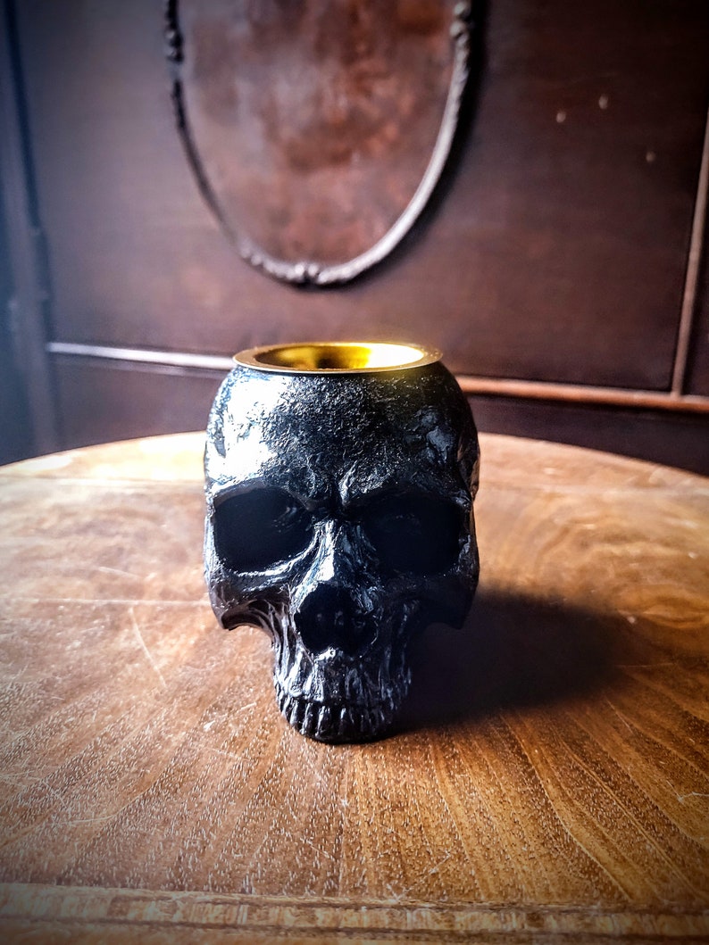 Pode incluir: Queimador de incenso de caveira preta com aro dourado. O queimador est&aacute; sobre uma mesa de madeira.