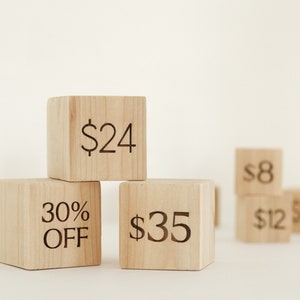 May include: Wooden blocks with prices and a discount written on them. The blocks are stacked on top of each other. The top block says £24, the middle block says 30% OFF, and the bottom block says £35.