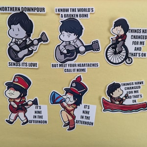 May include: A collection of cartoon stickers featuring musicians and song lyrics. The stickers depict characters playing guitars, in a wheelchair, and in a boat. Text includes "Northern Downpour", "Sends Its Love", and "Things Have Changed For Me And That's Ok".