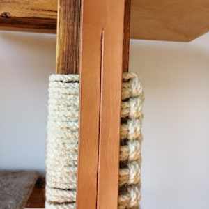 Pode incluir: Close-up de uma árvore de gato de madeira com uma correia de couro marrom e uma corda de fibra natural enrolada em torno do poste.