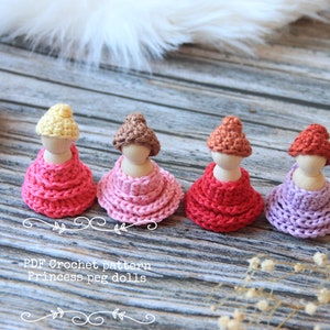 May include: Four handmade princess peg dolls with crochet dresses in shades of red, pink, and purple. Each doll has a wooden head and a crocheted hat. The text "PDF Crochet pattern Princess peg dolls" is visible.