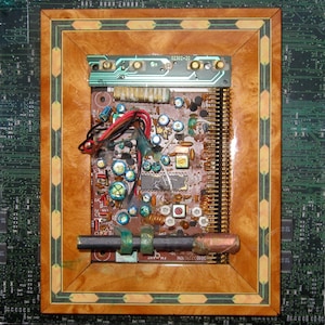 May include: A close-up of a circuit board with various electronic components, including resistors, capacitors, and integrated circuits. The board is framed in a wooden frame with a decorative border. The text "02302-20" is visible on the board.