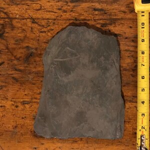 May include: A dark gray slate tile measuring approximately 6 inches by 8 inches. The tile is smooth and has a slightly rough texture.