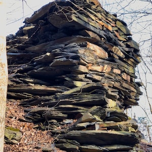 May include: A large pile of dark gray and brown slate rocks stacked on top of each other in a natural setting.