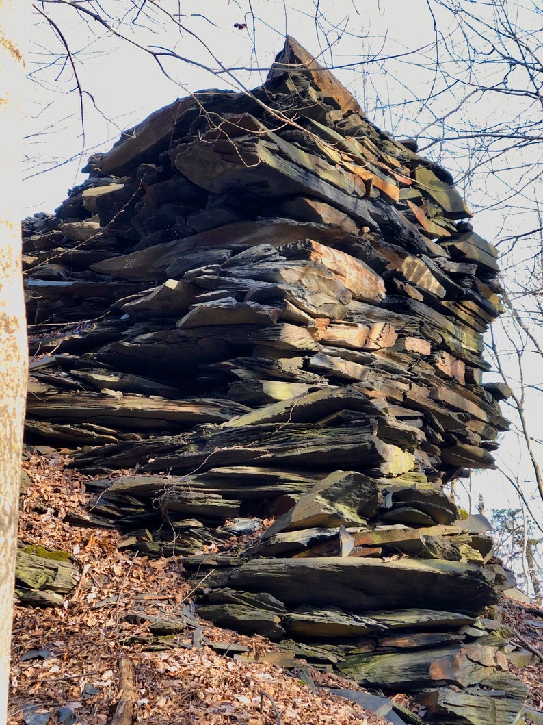 May include: A large pile of dark gray and brown slate rocks stacked on top of each other in a natural setting.