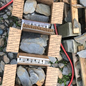 May include: Two cardboard boxes filled with various sizes of gray slate rocks. The boxes are labeled with "Priority Mail" and "Thank you for using Priority Mail Service".