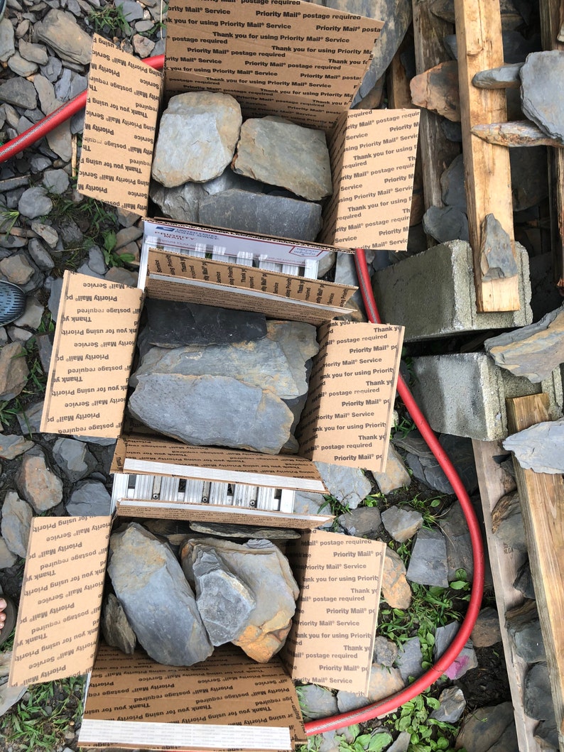 May include: Two cardboard boxes filled with various sizes of gray slate rocks. The boxes are labeled with "Priority Mail" and "Thank you for using Priority Mail Service".