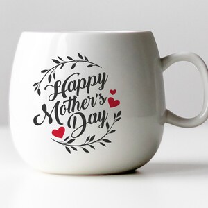 May include: White ceramic mug with a black and white design that says "Happy Mother's Day" with a wreath of leaves and three red hearts.