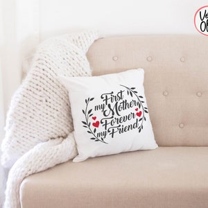 May include: White throw pillow with black text that reads "First my Mother Forever my Friend" with a wreath of leaves and red hearts around the text.